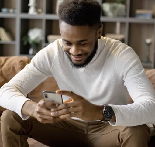 A man sitting on a coush texting on a mobile phone